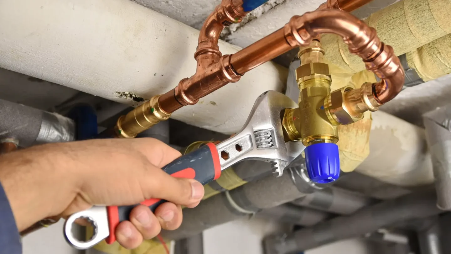 Installateur benutzt einen Schraubenschlüssel, um ein Ventil an komplexen Kupferrohren einer Warmwasseranlage festzuziehen.