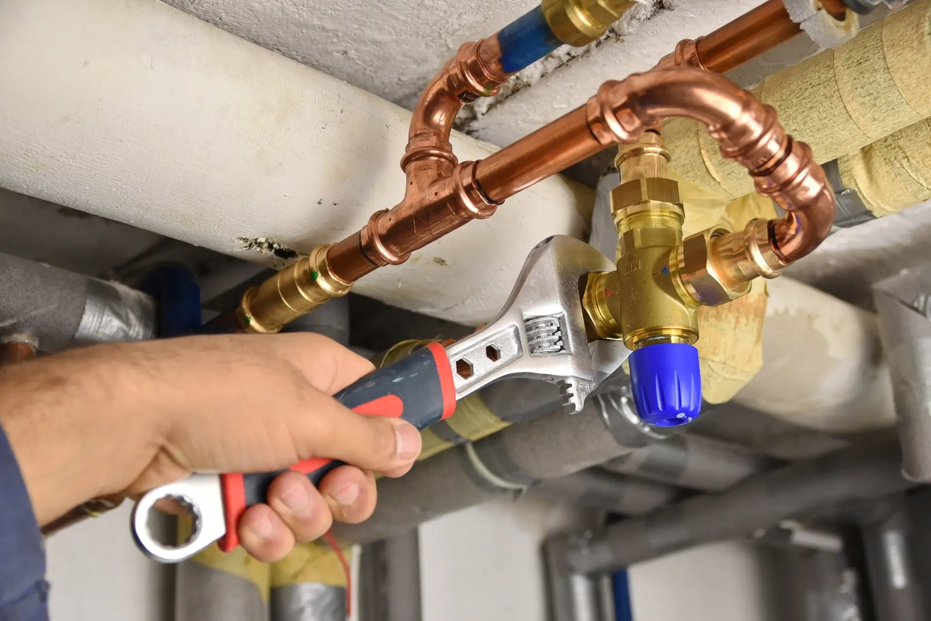 Installateur benutzt einen Schraubenschlüssel, um ein Ventil an komplexen Kupferrohren einer Warmwasseranlage festzuziehen.